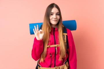 Young mountaineer girl with a big backpack isolated on pink background showing an ok sign with fingers