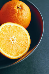 Fresh juicy oranges in black bowl, healthy diet and nutrition