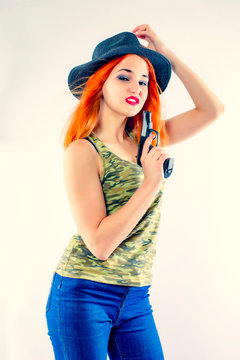 Young woman gangster with gun on a light background.Portrait of beautiful redhead girl in hat with gun.