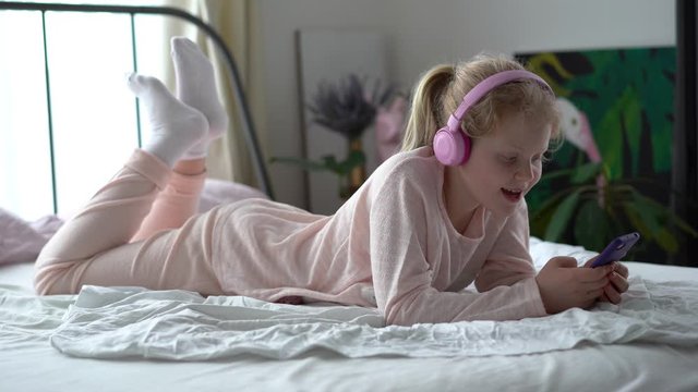modern life of generation Z. teenage girl in pajamas and headphones in the room on the bed listens to music from a smartphone.