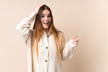 Young caucasian woman isolated on beige background surprised and pointing finger to the side