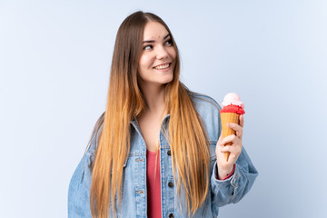Young woman with a cornet ice cream isolated on blue background looking up while smiling