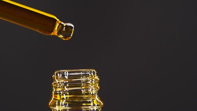 Close-up of of aromatheraphy oil drops dripping from dropper into a bottle, anti aging serum skin care