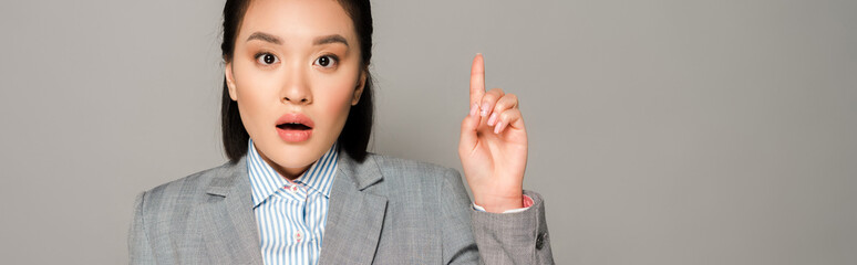 excited young businesswoman in suit showing idea gesture isolated on grey background, panoramic shot