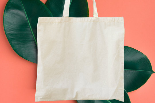 Blank cotton white shopper tote bag on pink background with green leaves. Mock up template for product branding plastic free reusable nature-friendly materials concept