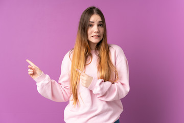 Young caucasian woman isolated on purple background frightened and pointing to the side