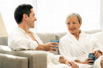 Middle aged couple sitting on couch in bathrobes.