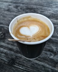 take away paper cup with cappuccino on wooden rustic background, heart shape in foam