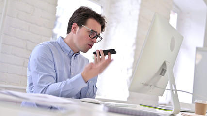 Angry Working Young Man Talking on Smart Phone in Office