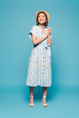 smiling brunette asian girl in striped dress and straw hat on blue background