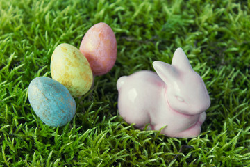 Easter composition with porcelain bunny rabbit and three Easter eggs on green moss.