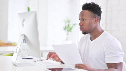 Casual African Man doing Paperwork with Desktop in Office