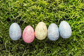 Five decorative Easter eggs arranged in a row on green moss background.