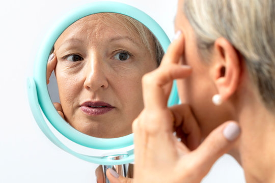 Middle Aged Woman Reviewing Wrinkles In Hand Mirror.