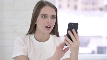 Fototapeta na wymiar Surprised Young Woman Excited for Success on Smartphone