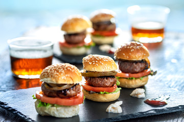 Multiple mini beef hamburgers with small beers.