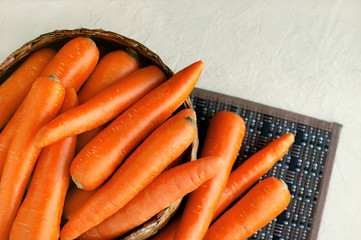 Fresh carrots in a basket on a textural background. A lot of carrots in a basket on a bamboo napkin. Orange vegetables for a healthy diet.