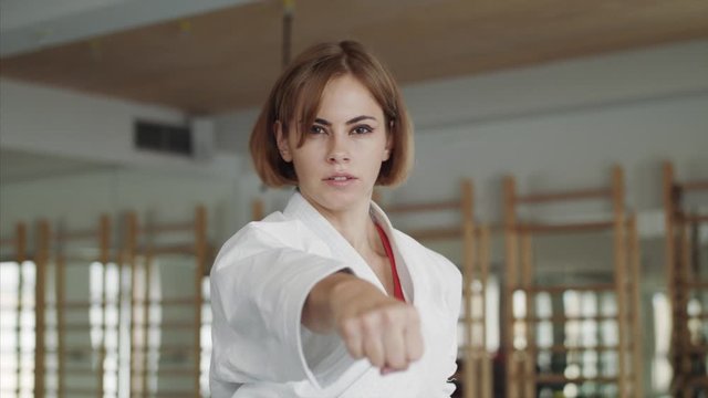 Young woman practising karate indoors in gym.