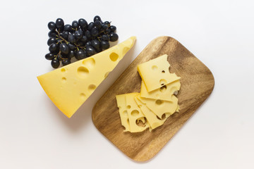 Large piece of Maasdam cheese on wooden board with dark blue grapes on white background.
