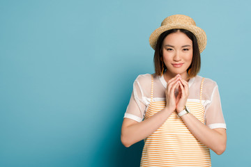 cunning asian girl in striped yellow dress and straw hat on blue background