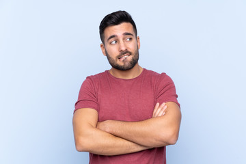 Young handsome man with beard over isolated blue background with confuse face expression