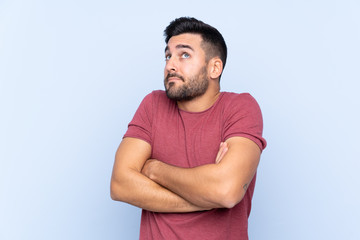 Young handsome man with beard over isolated blue background making doubts gesture while lifting the shoulders