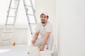 A male painter in a white uniform with a roller works in his hand in a white room