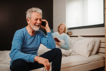 Close photo of grey haired elderly man talking over the phone and holding eyeglasses.