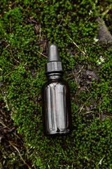 Bottle of serum on dark background from moss
