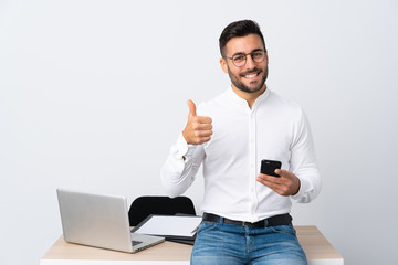 Young businessman holding a mobile phone giving a thumbs up gesture
