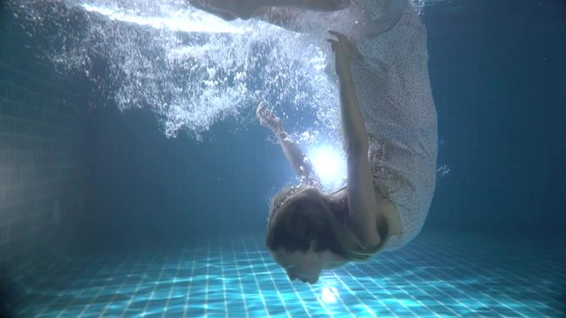Beautiful woman with long red hair swimming underwater in dress - video in slow motion