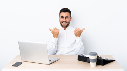 Young businessman in a workplace with thumbs up gesture and smiling