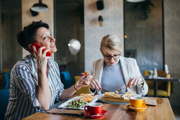 women friends having lunch break in restaurant, using mobile phone
