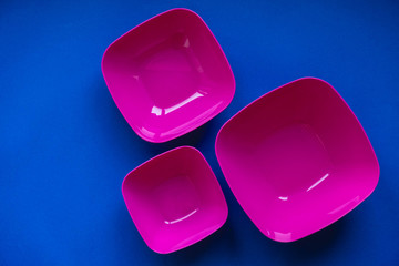 Set of pink plates on blue background. Plastic utensils for the kitchen. Top view. Minimalist Style. Copy, empty space for text