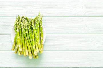Fresh asparagus on plate on green wooden background top-down copy space