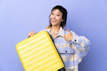 Young Uruguayan woman over isolated purple background in vacation with travel suitcase and with thumb up