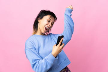 Young Uruguayan woman over isolated pink background with phone in victory position