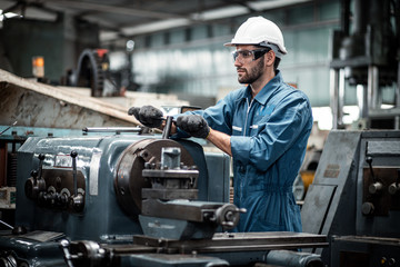 Men industrial engineer wearing a white helmet while standing in a heavy industrial factory behind....