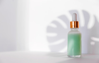 Natural cosmetics: serum with dropper and shadow from monstera  leave on white background.