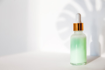 Natural cosmetics: serum with dropper and shadow from monstera  leave on white background.