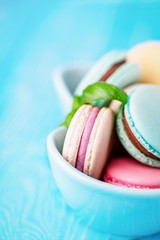 Turquoise bowl of french colorful macaroons or macarons on turquoise wooden background