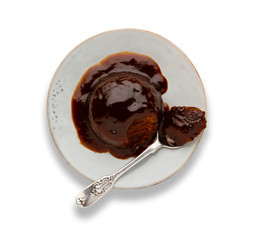 An individual sticky toffee sponge cake, with a sticky toffee sauce, on a white plate with a spoon, isolated on white.