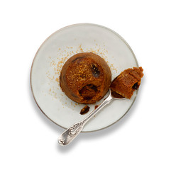 An individual spotted dick sponge cake, on a white plate with a spoon, isolated on white.