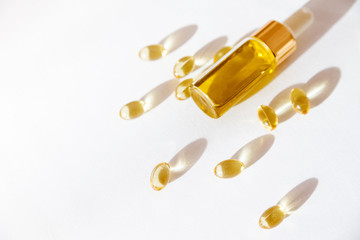 Natural cosmetics concept, essential oil in glass bottle with dropper and vitamin pills on white background