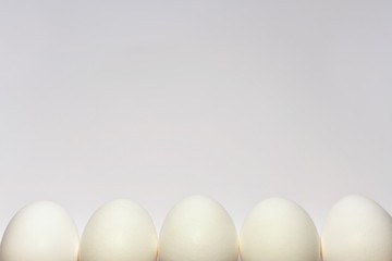 White chicken eggs lined up in a row half peeping out of the bottom edge of the frame on a light background.