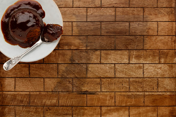An individual sticky toffee sponge cake, with a sticky toffee sauce, on a white plate with a spoon, on a checked wooden surface with space for copy