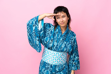 Young woman wearing kimono over isolated blue background looking far away with hand to look something