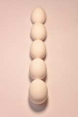 A vertical line in the center of oval chicken eggs lined up by a chain in a bed pink peach color.
