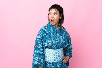 Young woman wearing kimono over isolated blue background doing surprise gesture while looking to the side