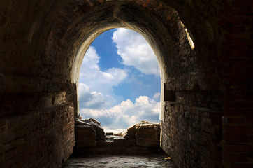 Fototapeta na wymiar The ancient tunnel, aged construction of historical fortress with cloudy blue sky background; Dark inside. Freedom at the end of tunnel.